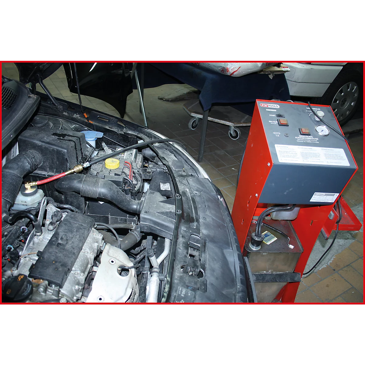 Ein offener Motorraum mit angeschlossenen Messgeräten und einer roten, grauen Apparatur. Im Hintergrund ein weiterer Wagen.